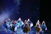 [Bildet viser 11 dansere som står barføtt på tå på scenen. De står under stjernehimmel, holder hendene i store havgrønne skjørt og ser oppover.] 