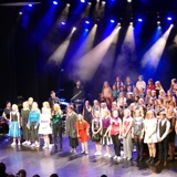 Bilde viser en masse barn og unge der står på scenen i vågensalen til en konsert.