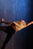 Bildet viser en danser på scenen som lever seg til gulvet med den ene armen og strekker ut den andre armen. Hun strekker beina ut motsatt vei. 